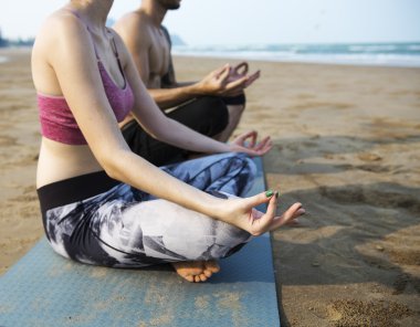 Çiftler plajda yoga yapıyor.