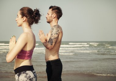 Çiftler plajda yoga yapıyor.