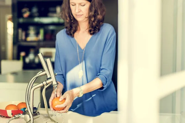 Женщина стирает оранжевый на кухне — стоковое фото
