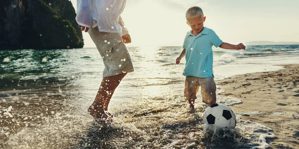 Far och son som spelar fotboll på stranden — Stockfoto