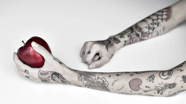 Hands in tattoos holds apple — Stock Photo, Image