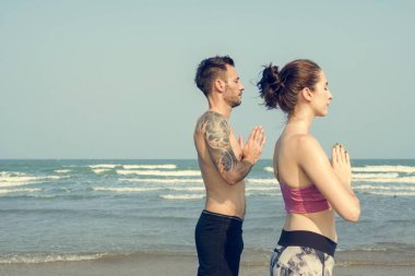 Çiftler plajda yoga yapıyor.