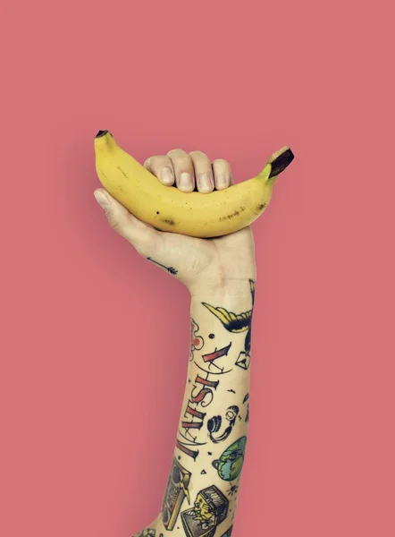 Hand in tattoos holds banana — Stock Photo, Image