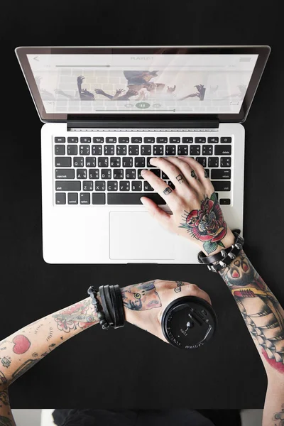 Руки в татуюваннях, що друкуються на ноутбуці — стокове фото