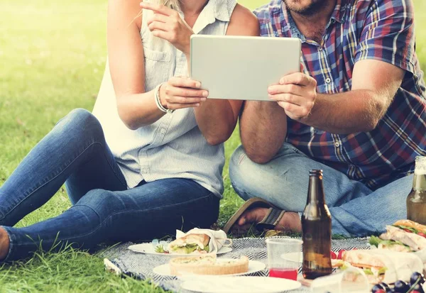Met behulp van digitale tablet op picknick (echt) paar — Stockfoto