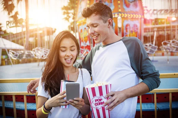 Pareja usando móvil en parque de atracciones — Foto de Stock