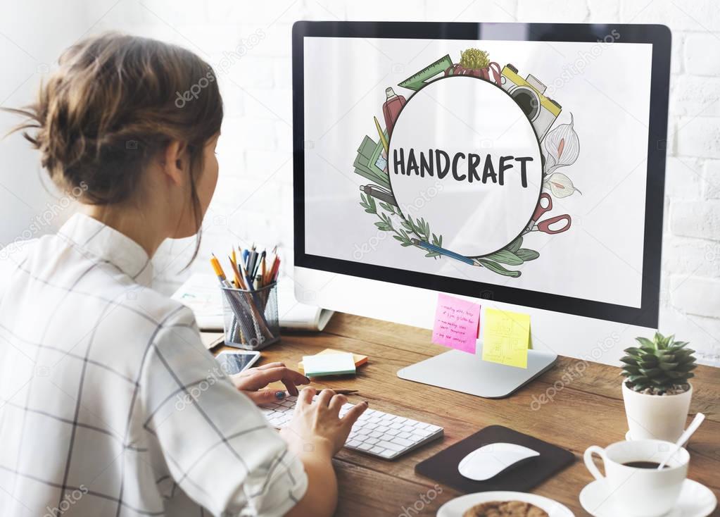 Woman working with computer at workplace table with office tools, coffee cup, little house plant and keyboard, text on monitor screen: Handcraft