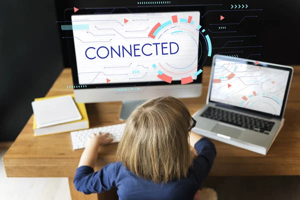 Menina sentada à mesa contra computador — Fotografia de Stock