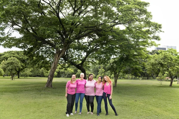 women in pink blouses embracing in front of park