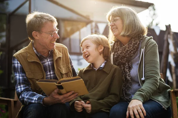 Senior couple reading book with grandson — Stock Photo, Image