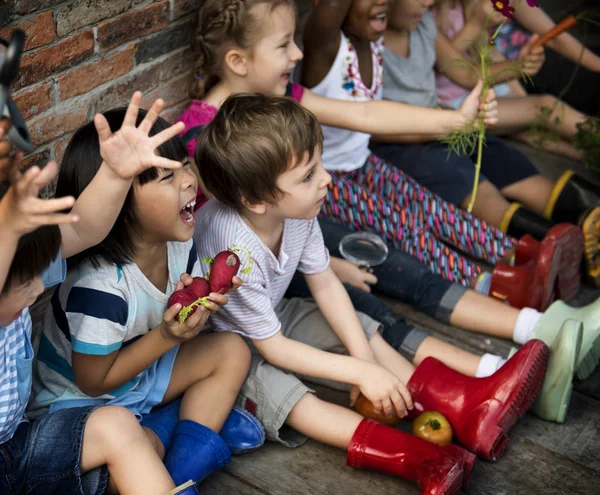 Grupo de niños del jardín de infantes que se sientan cerca de la pared de ladrillo — Foto de Stock