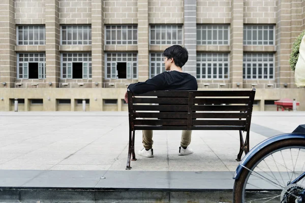 Mężczyzna siedzący na ławce przed budynkiem — Zdjęcie stockowe