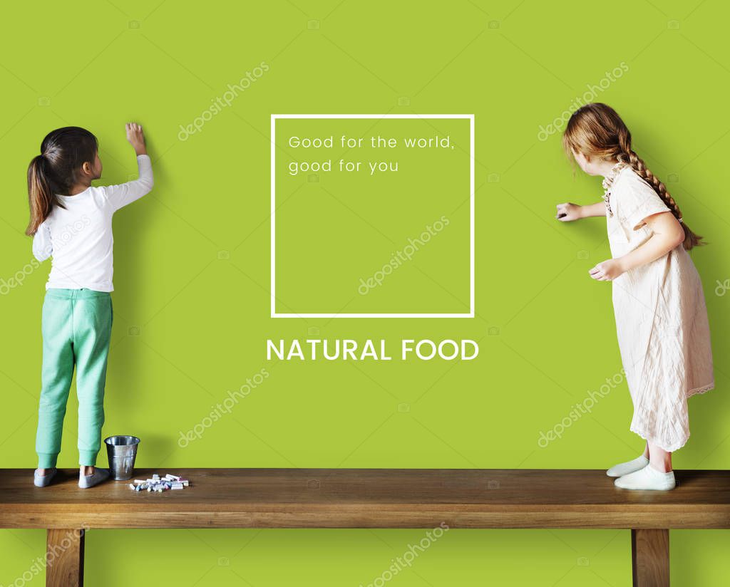 Two little girls standing on the table and drawing on the green wall with inscription: Natural Food