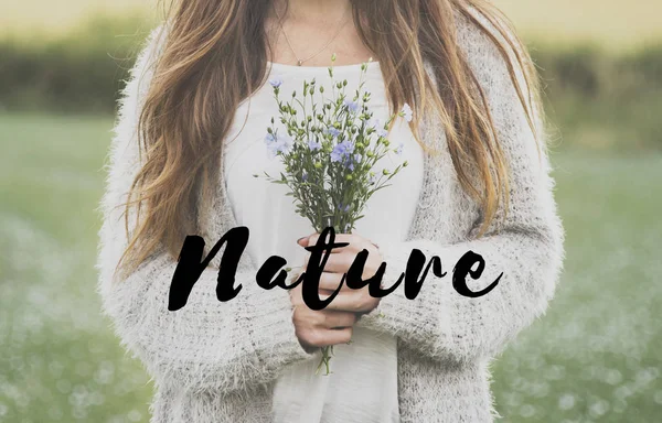 Woman standing in field and holding flowers — Stock Photo, Image