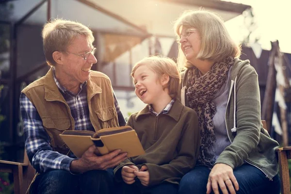 Senior couple reading book with grandson — Stock Photo, Image