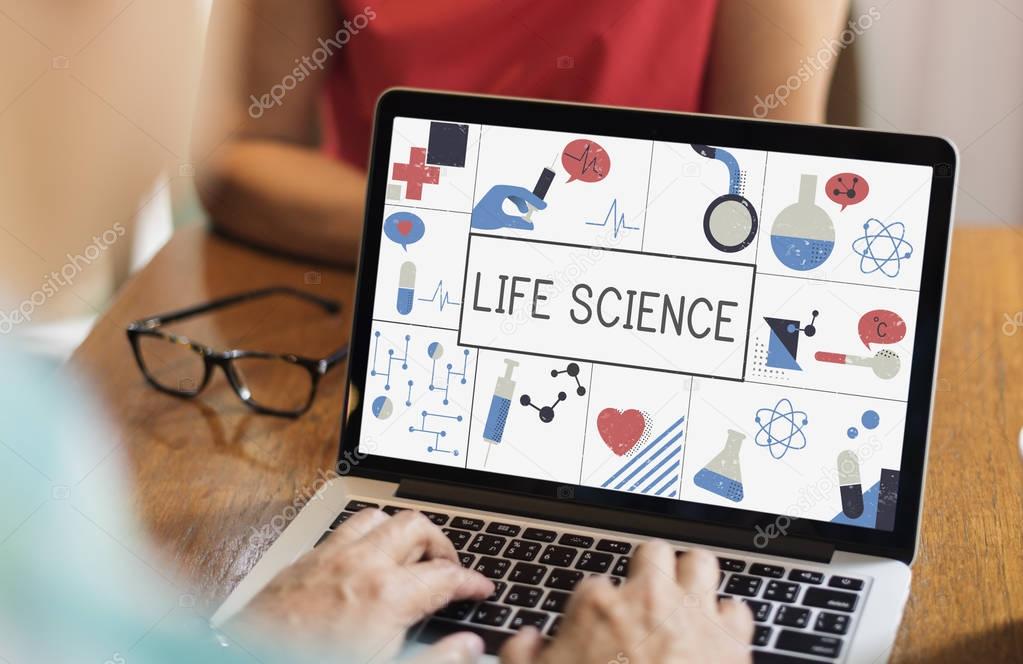 Man typing on laptop keyboard in front of sitting woman, monitor screen with title: Life Science