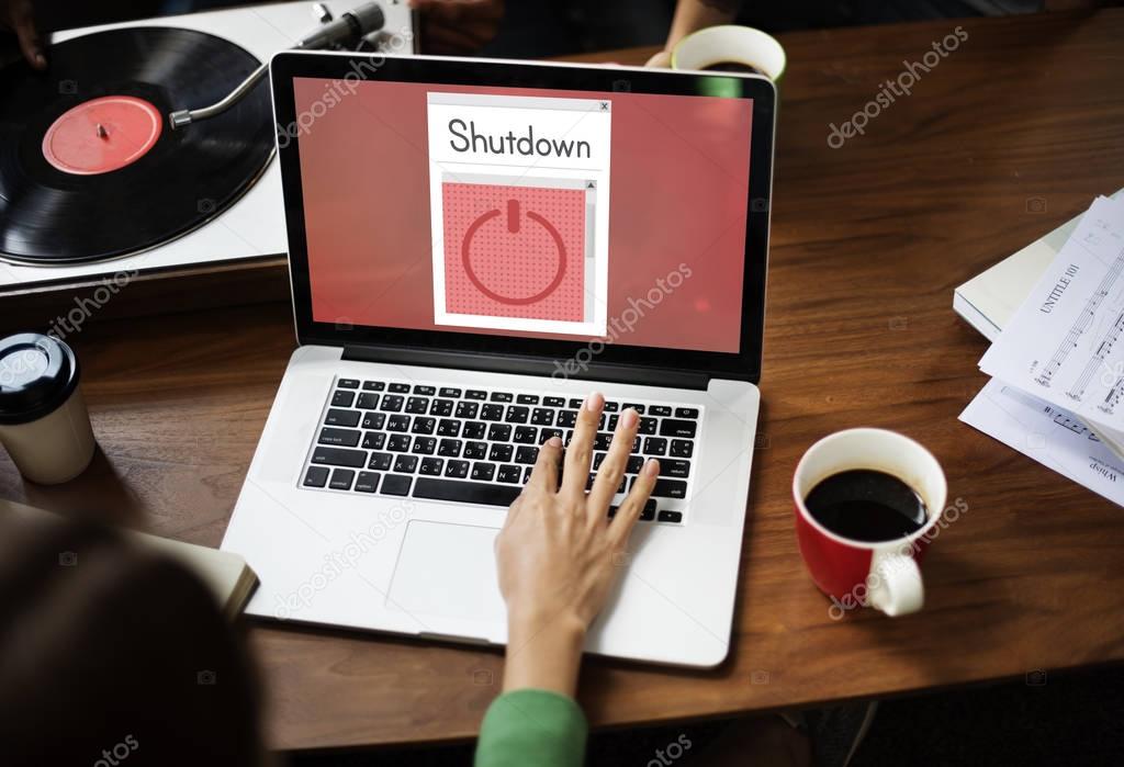 Woman typing on laptop keyboard at table with coffee cup and vinyl player, monitor screen with title: Shutdown