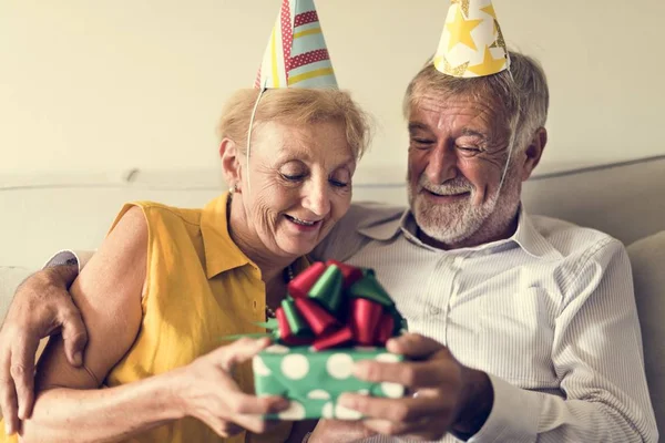 Couple in party hats holding gift — Stock Photo, Image