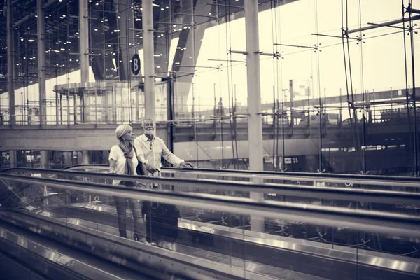 Ανώτερος ζευγάρι στέκεται σε κυλιόμενες σκάλες στο αεροδρόμιο — Φωτογραφία Αρχείου