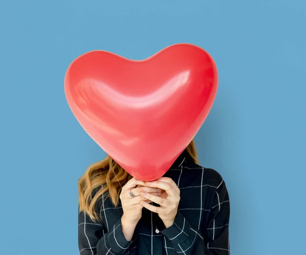 Woman covering face with heart balloon
