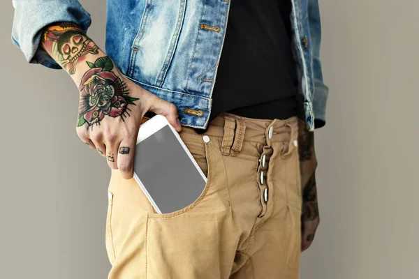 Татуированная рука кладет мобильный телефон в карман — стоковое фото