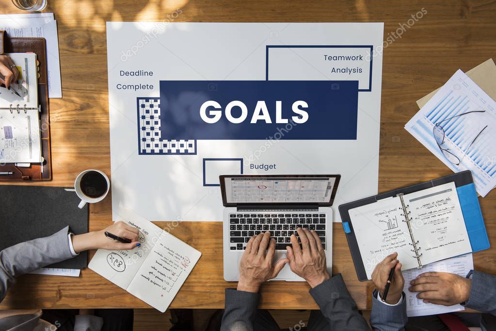 Hands of business people over wooden table and banner with Goals