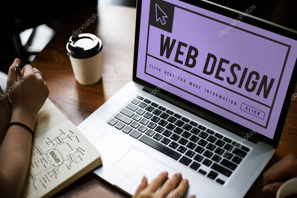Workplace table with laptop, partial view of people hands working and writing notes in diary, monitor screen with title: Web Design
