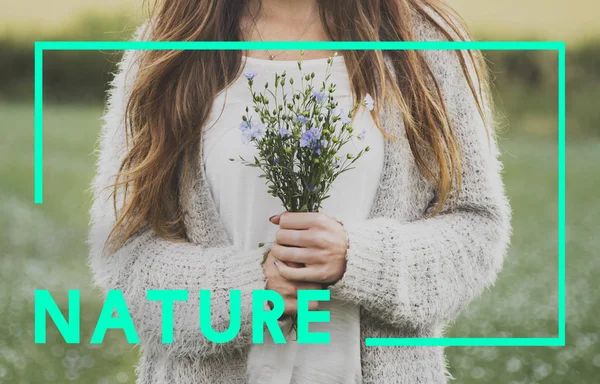 Woman standing in field and holding flowers — Stock Photo, Image