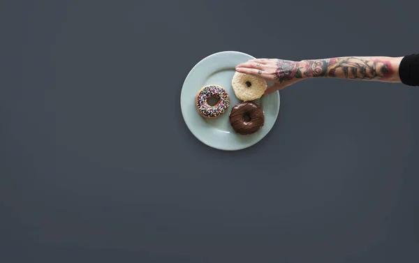 Hand med tatueringar att nå donut — Stockfoto