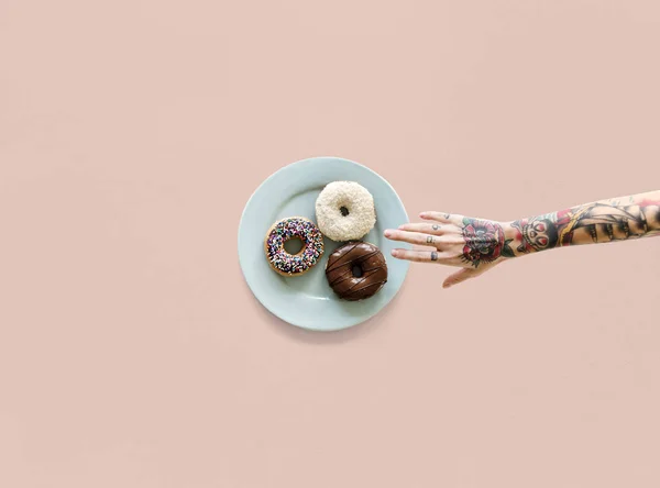 Hand med tatueringar att nå donut — Stockfoto