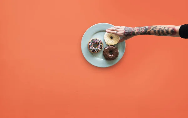 Hand med tatueringar att nå donut — Stockfoto