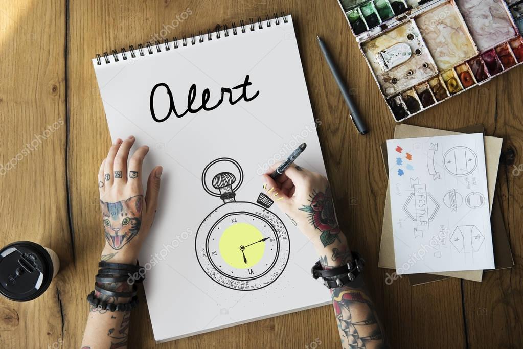 Tattooed person drawing in notepad on wooden table. Alert  concept