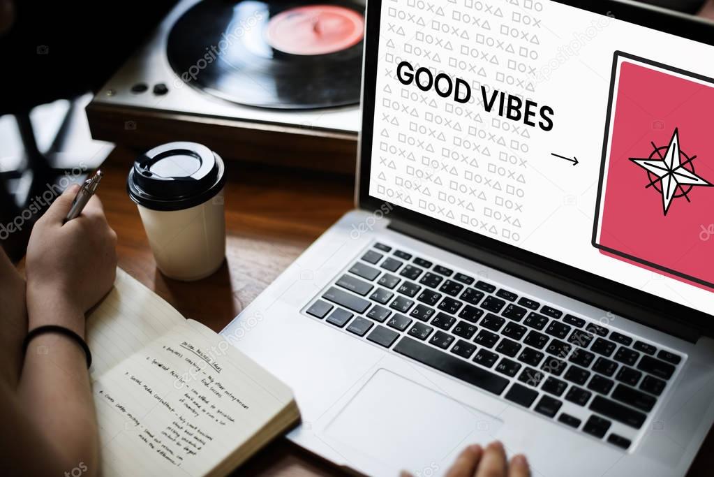People working with laptop, person writing notes in diary, coffee mug and vinyl player on table, text on screen: Good Vibes