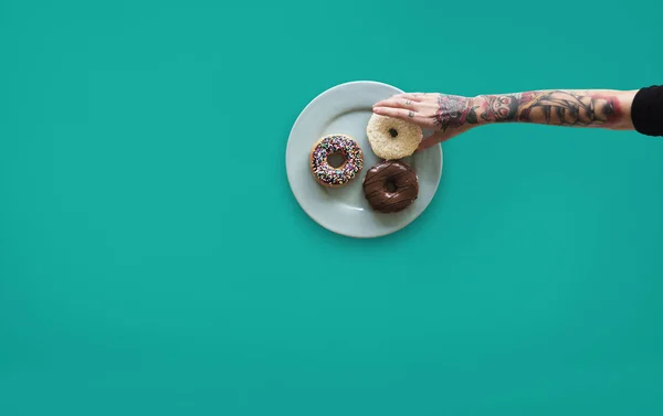 Mano con tatuajes alcanzando para donut — Foto de Stock