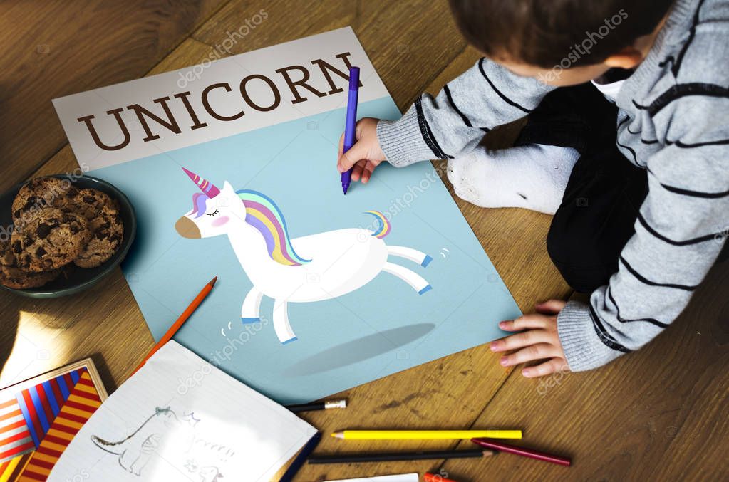 Little boy drawing on album paper while sitting on floor, text: Unicorn