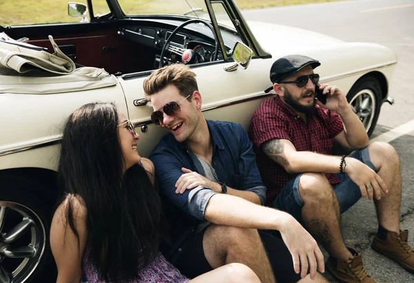 Yolda arabanın yanında oturan arkadaşlar