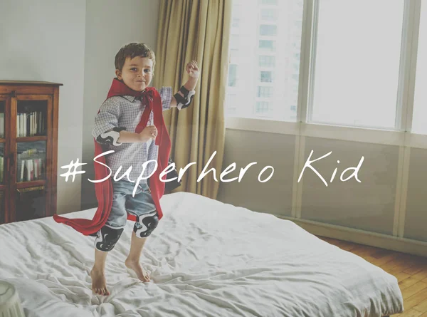 Menino no traje de super-herói pulando na cama — Fotografia de Stock