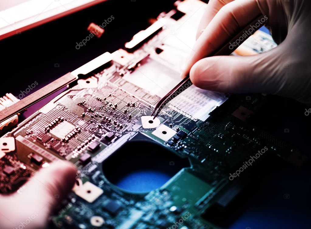 Closeup of hands with computer motherboard and tweezers