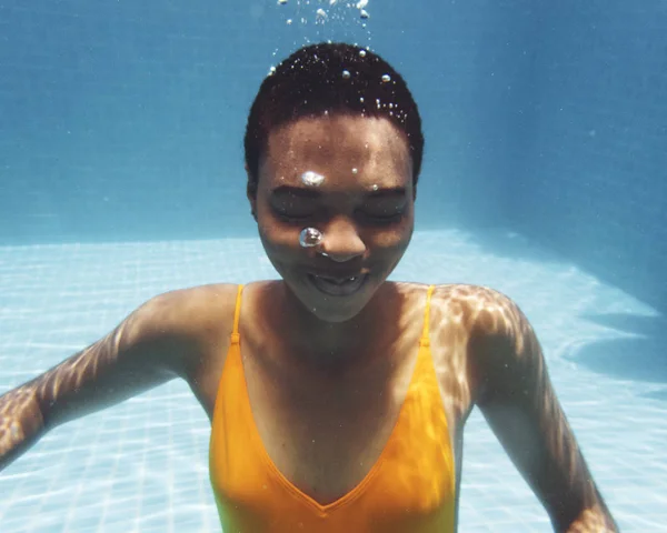 Mujer afrodescendiente sonriendo bajo el agua en la piscina —  Fotos de Stock