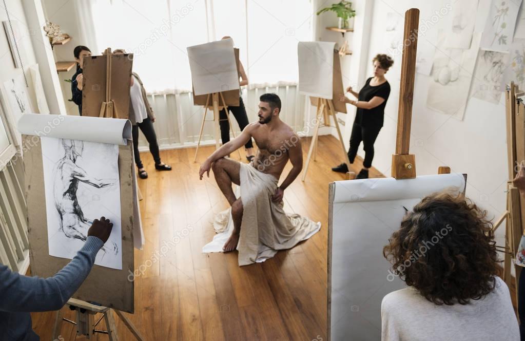 People drawing from nude male model in art studio