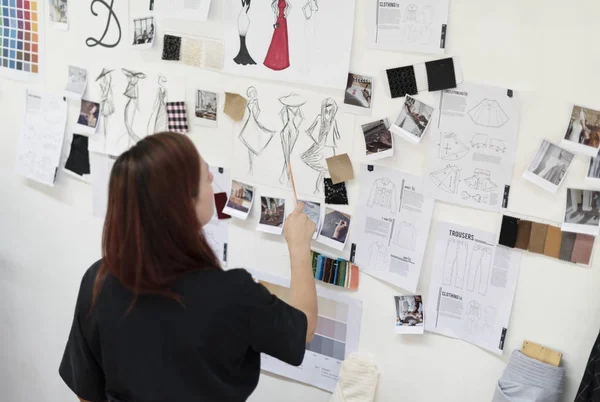 Woman looking to sketches of clothing on wall in sewing studio, original photoset