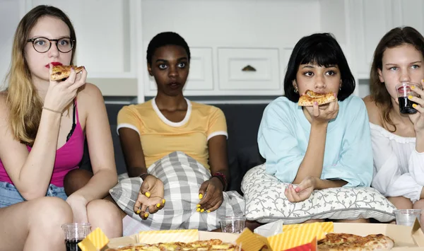 A group of diverse women sitting on the couch and eating pizza together, original photoset