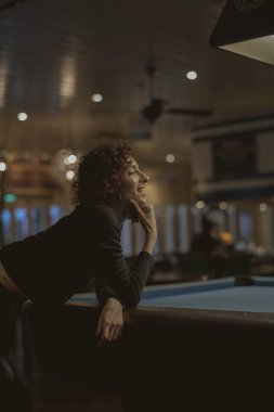 Bilardo masası üzerinde yaslanmış kısa saç kesimi ile ince kadın  