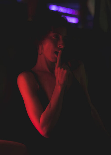 Portrait of woman showing a seductive gesture in a dark bar with red light    