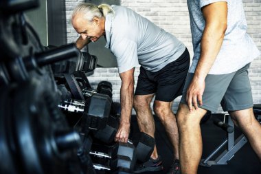 Elderly man taking barbell at fitness gym  clipart