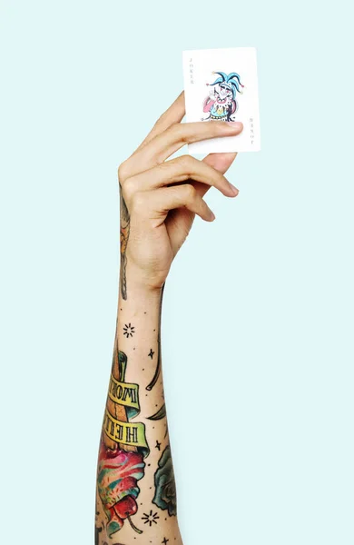 Mano Humana Con Tatuajes Contra Fondo Azul Sosteniendo Tarjeta Joker — Foto de Stock
