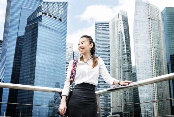 亚洲女商人在摩天大楼的背景下微笑着站在栏杆旁 — 图库照片