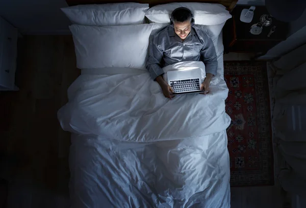 Άντρας Στο Κρεβάτι Χρησιμοποιώντας Φορητό Υπολογιστή Στα Ακουστικά — Φωτογραφία Αρχείου
