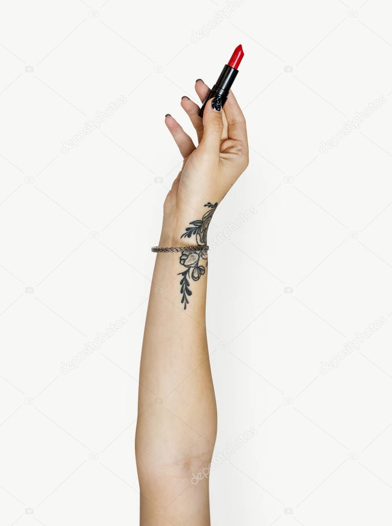 human hand with tattoos against white background holding red lipstick 