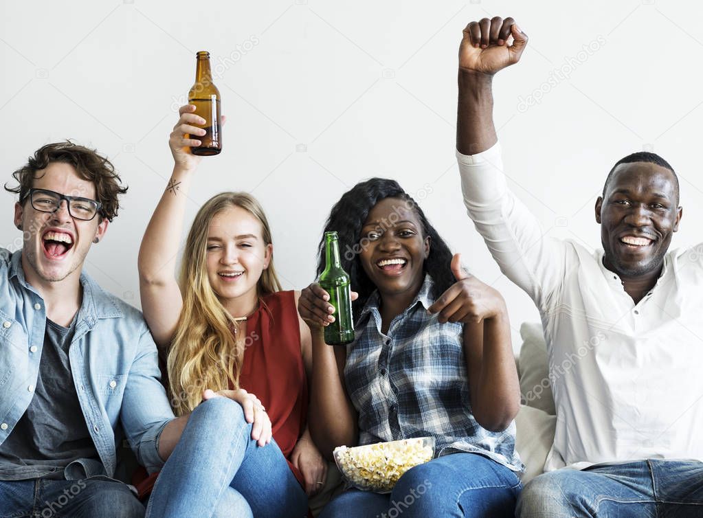 Group of diverse friends drinking and cheering while watching sports together